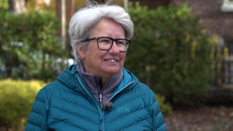 Plan rapproché d'Agnès Maltais, à l'extérieur. Elle porte un manteau bleu et des lunettes.