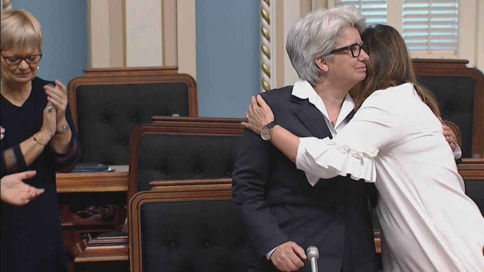 Agnès Maltais reçoit l’accolade de sa collègue Diane Lamarre à la suite de sa dernière intervention en carrière à l’Assemblée nationale. Un peu en retrait, la députée Lorraine Richard applaudit.