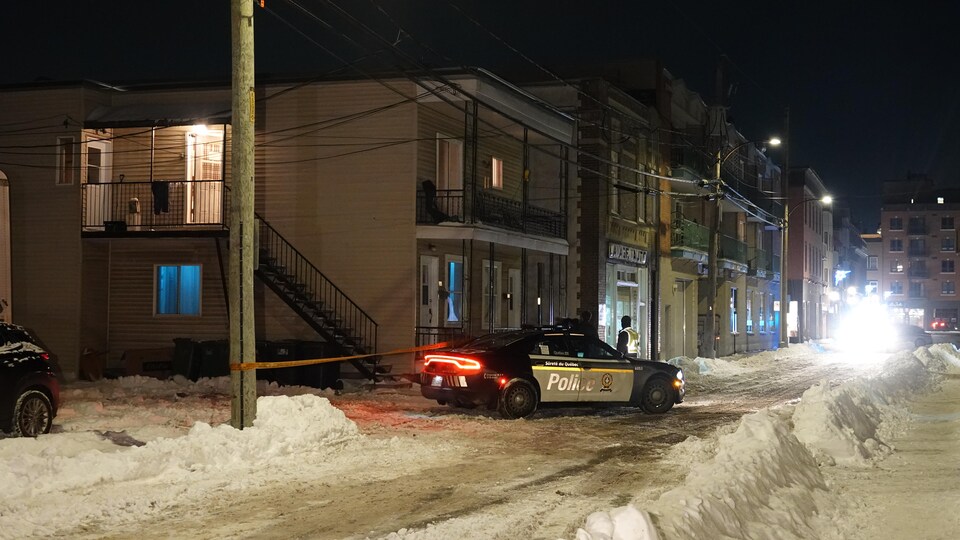 Un véhicule de la Sûreté du Québec dans une rue enneigée, devant un scène de crime.