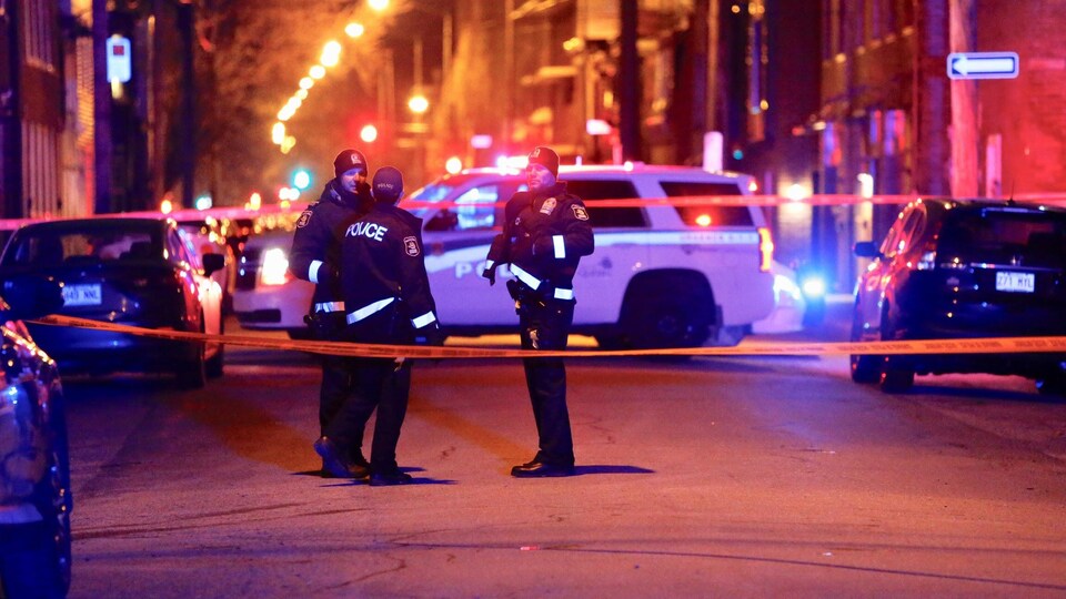 Trois policiers sont derrière le cordon de sécurité.