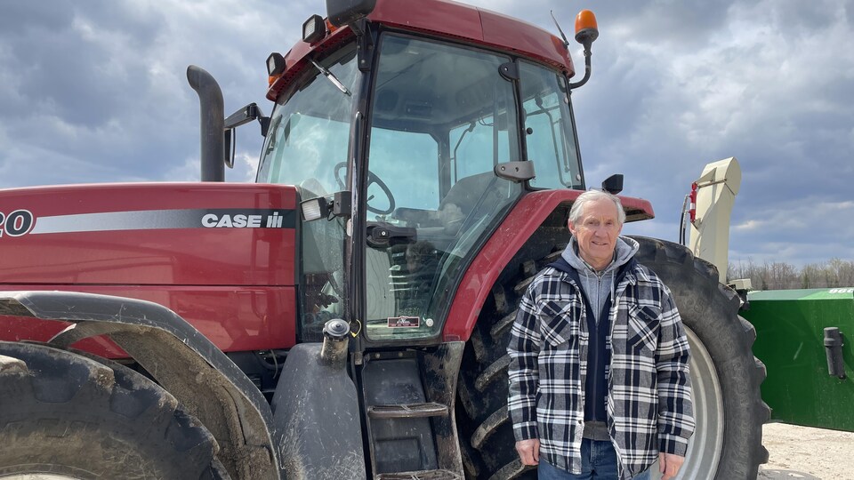 Un agriculteur devant son tracteur qui sourit.