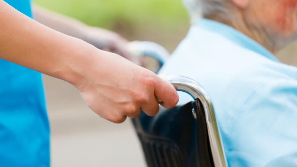 Une infirmière pousse une chaise roulante.