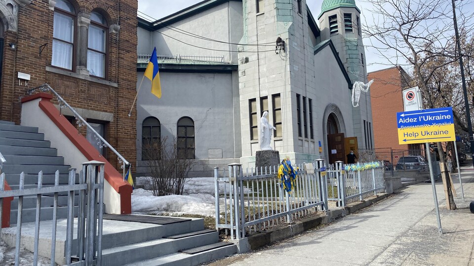 Une église ukrainienne devant laquelle se trouve une affiche bleu et jaune sur laquelle il est écrit : « Aidez l'Ukraine, Help Ukraine ».