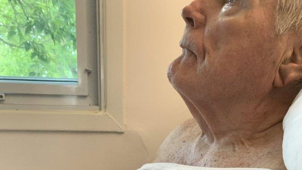 Le père de Jacy Ruuhala dans son lit avec la poitrine nue couverte uniquement d'une serviette humide.