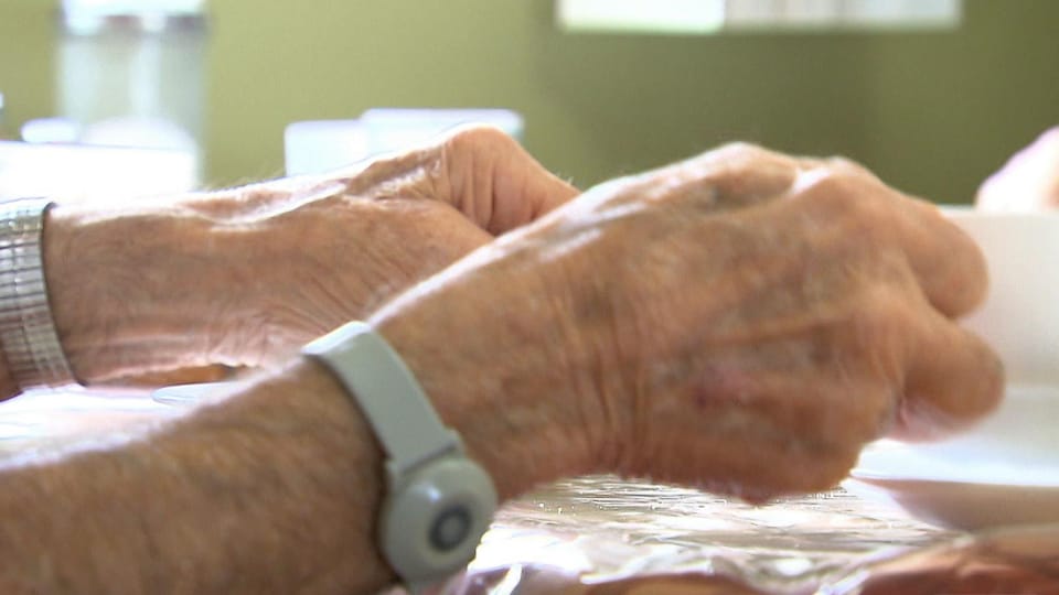La caméra montre en gros plan les mains d'une personne âgée qui s'affaire à une table.