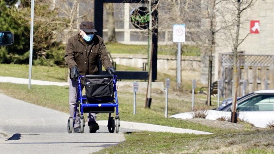 Une personne âgée marche sur le trottoir à l'aide d'un déambulateur.