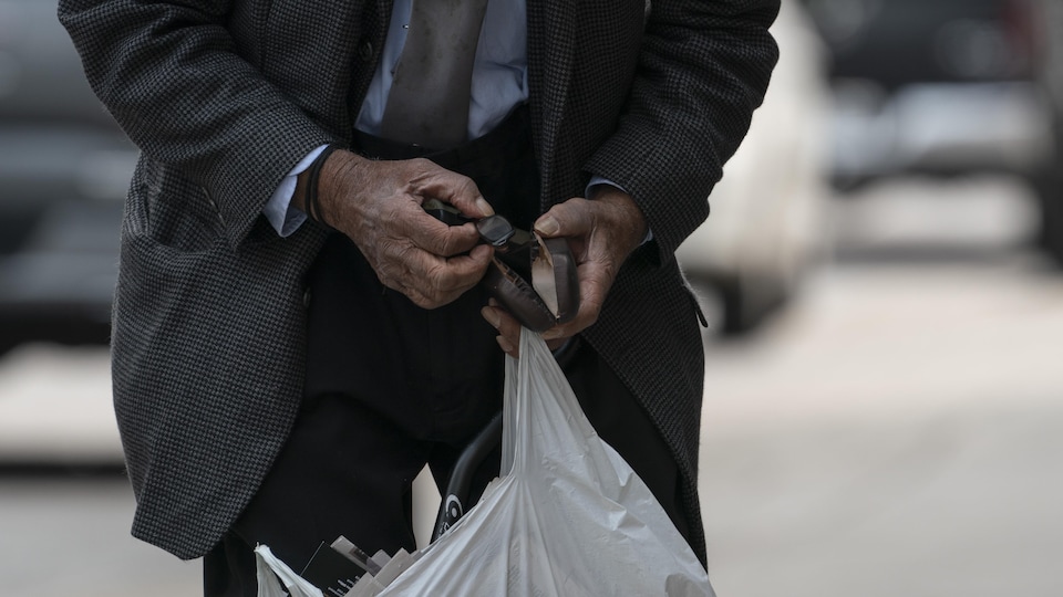 Les mains d'un homme âgé tenant des lunettes et un sac de plastique blanc.