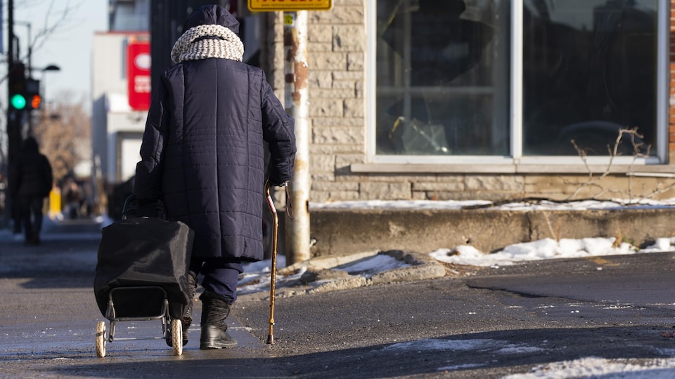 Une personne âgée marche avec une canne en tirant un chariot rue Ontario, à Montréal.
