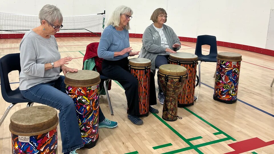 Trois femmes assises jouent au tambour dans un gymnase.
