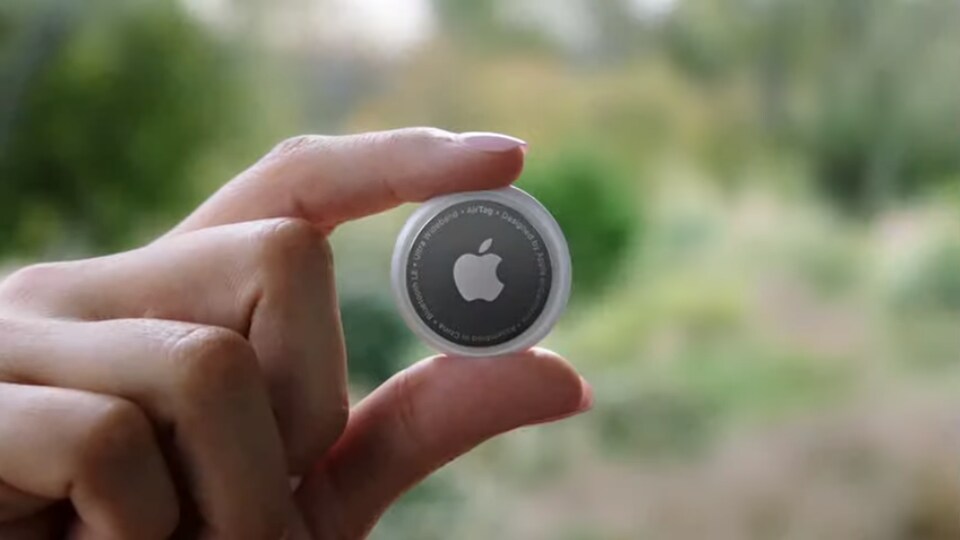 Une main qui tient un objet rond à l'effigie du logo d'Apple. 