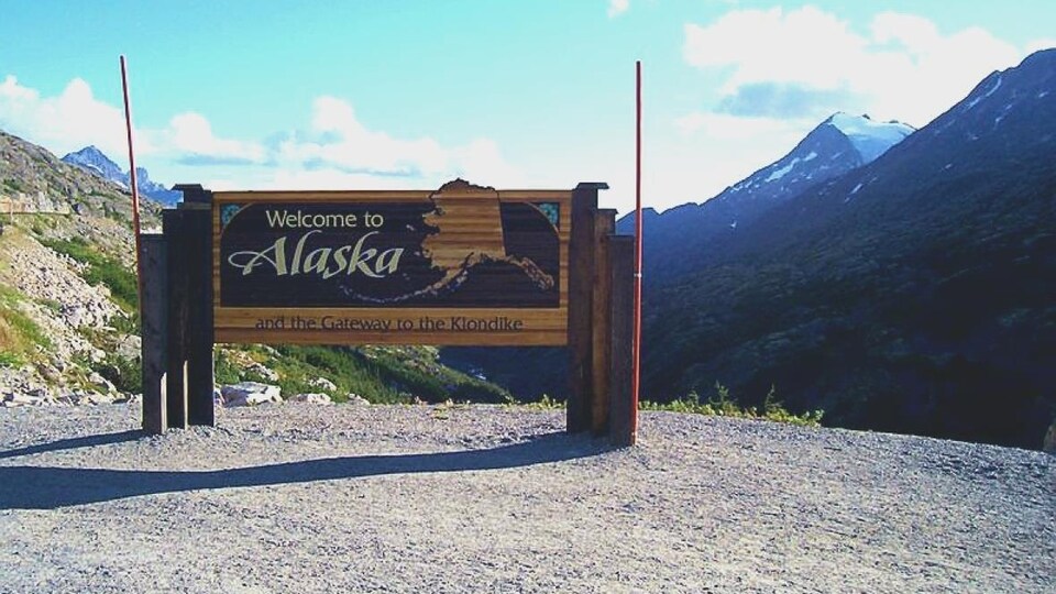 Panneau de bienvenue en Alaska devant des montagnes en été.