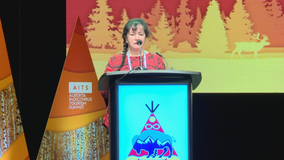 Une femme parle à un podium sur lequel il y a un dessin de bison et un tipi.