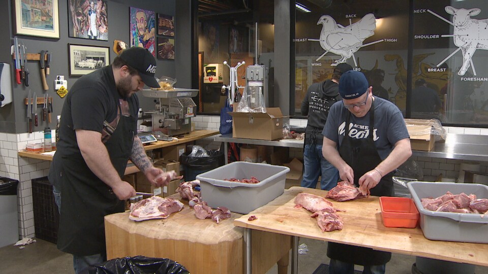 Un boucher découpe de la viande dans la boucherie Acme Meats.
