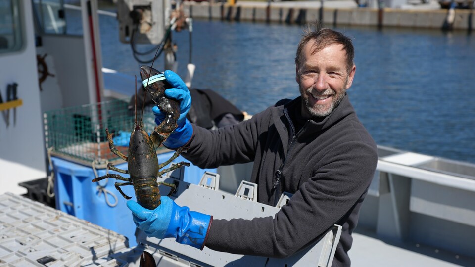 Le pêcheur Albini Lelièvre, tout sourire, tend un homard pour le montrer à la caméra.