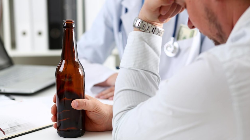 Un homme qui tient une bouteille de bière se trouve devant un médecin.