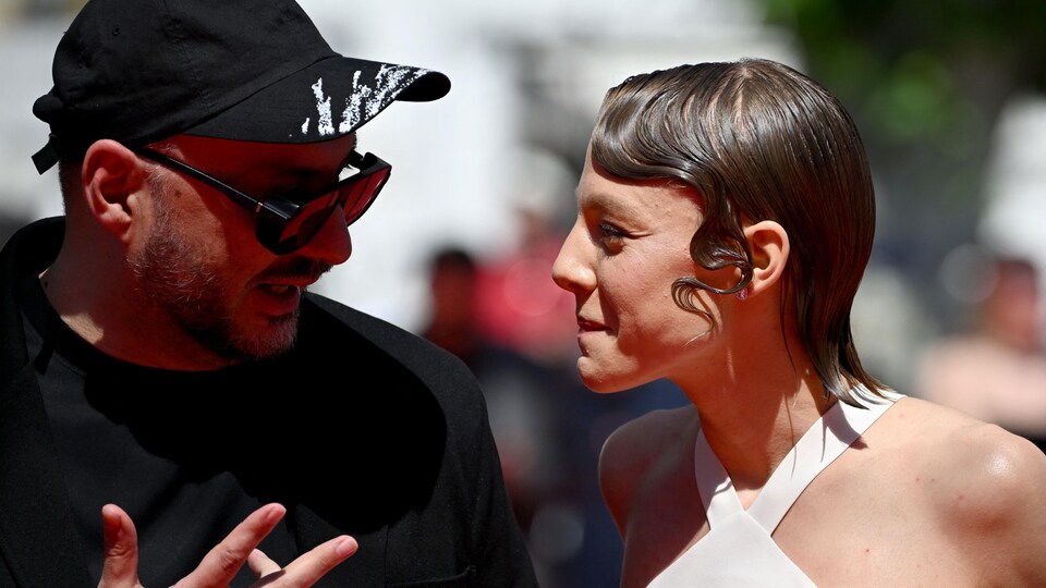 A man and a woman, in profile, converse on the red carpet of the Cannes Film Festival. 