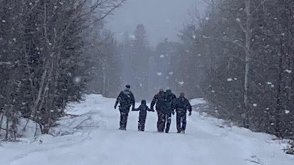 Des policiers marchent dans la neige en compagnie d'un enfant.