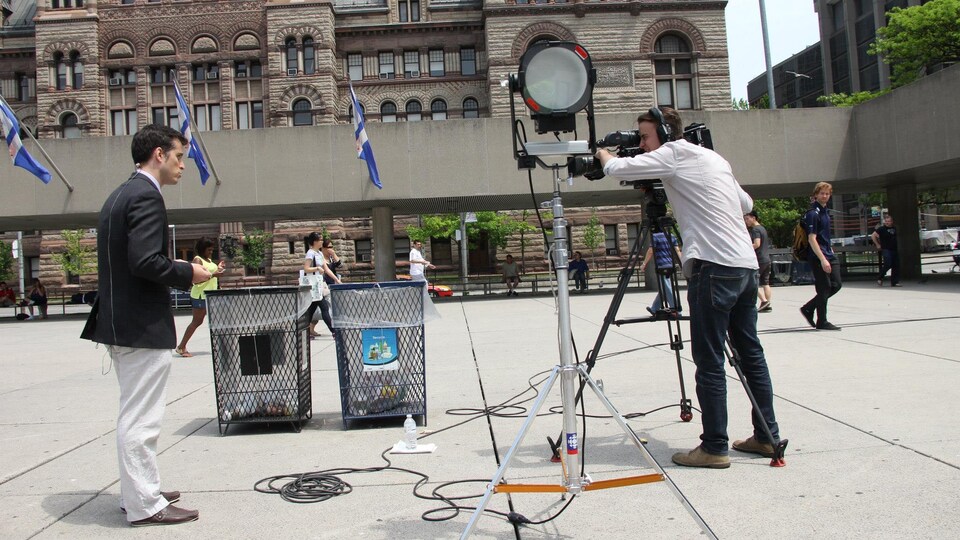 Le journaliste Alex Boissonneault devant une caméra sur une place publique.