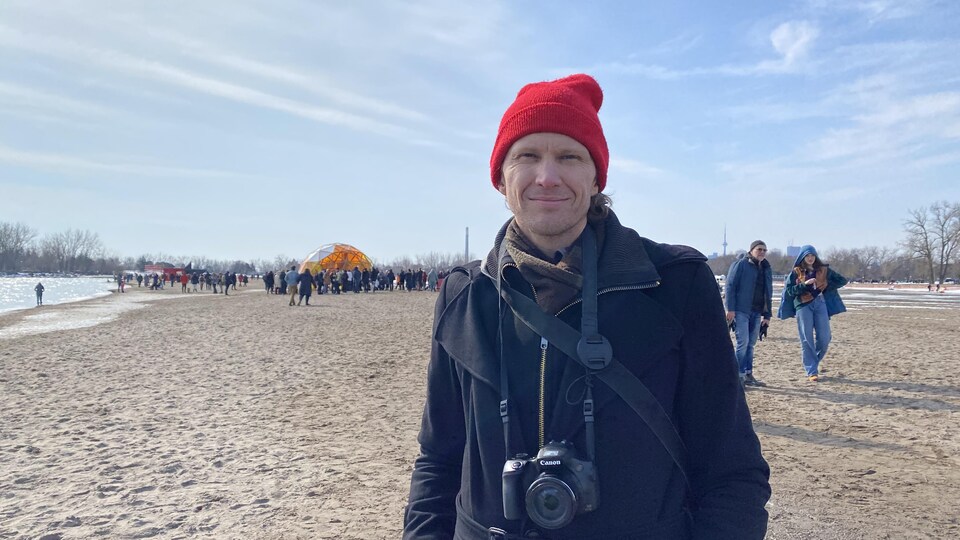 Alex Eddington sourit à la caméra. Il se situe sur la plage.