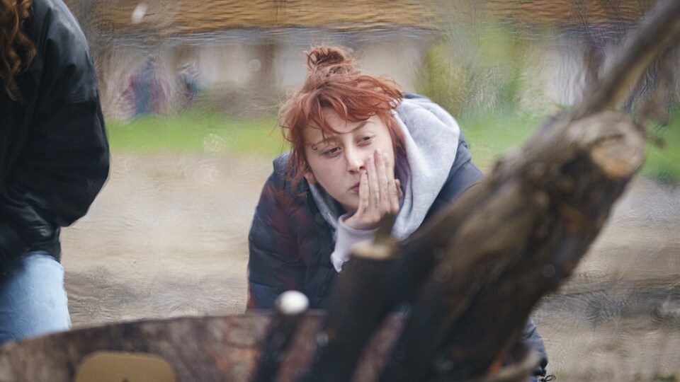 Une femme assise près d'un feu regarde au loin.