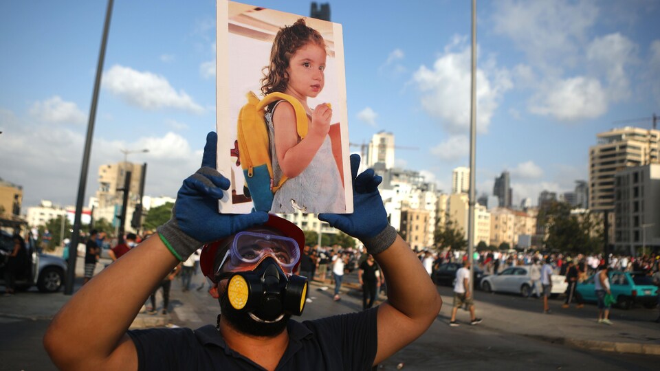 Un homme portant un masque tenant une large photo d'une fillette dans ses bras.