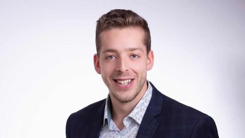 Alexandre Cédric Doucet souriant à la caméra en complet veston.