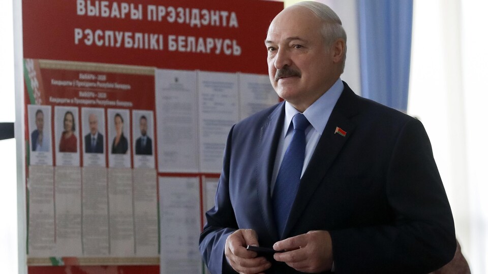 Alexandre Loukachenko, devant une affiche des candidats à la présidentielle.