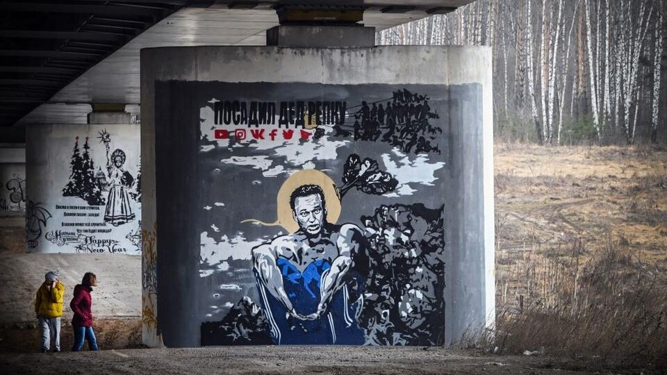 Deux personnes passent devant l'immense murale peinte sur l'un des piliers d'un viaduc.