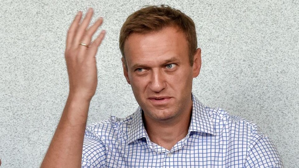 Alexeï Navalny, faisant dos à un mur, a la main droite levée à hauteur de son visage.