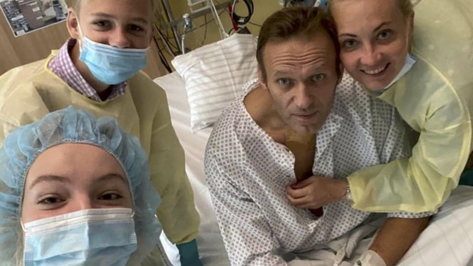 Un homme prend la pose à partir d'un lit d'hôpital avec son épouse et ses deux enfants.