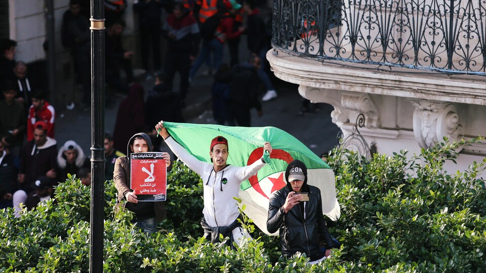 Trois hommes manifestent avec un drapeau et une affiche.