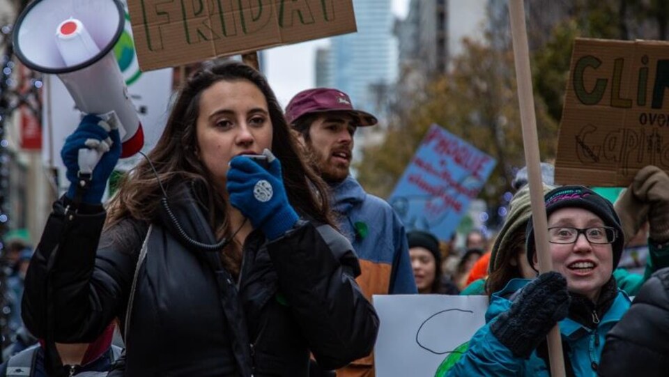 Un femme qui tient un mégaphone en marchant avec des centaines de jeunes qui militent pour l'environnement.