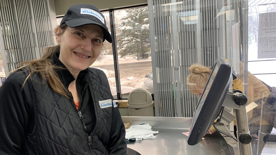 Une femme sourit derrière une caisse d'épicerie.