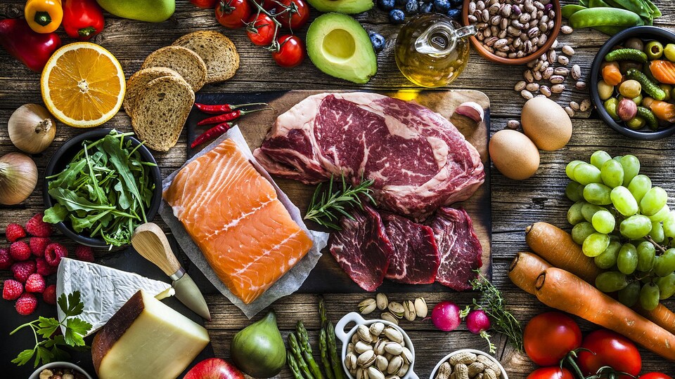 Une table montrant une grande variété d'aliments comme des fruits, des légumes, du fromage, du pain, des œufs, des légumineuses, de la viande et des noix.