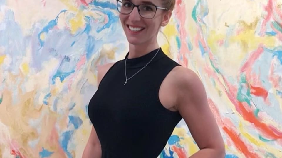 Une femme en robe noire devant un mur coloré.