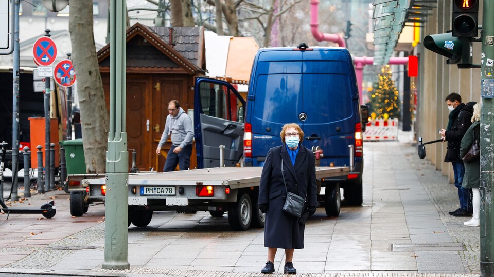 Une vielle femme attend au feu de circulation, devant le marché.