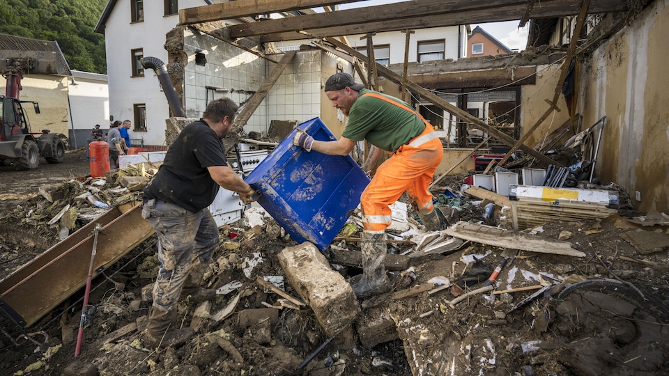 Des habitants transportent une boîte à l’extérieur d'une cuisine détruite par des inondations
