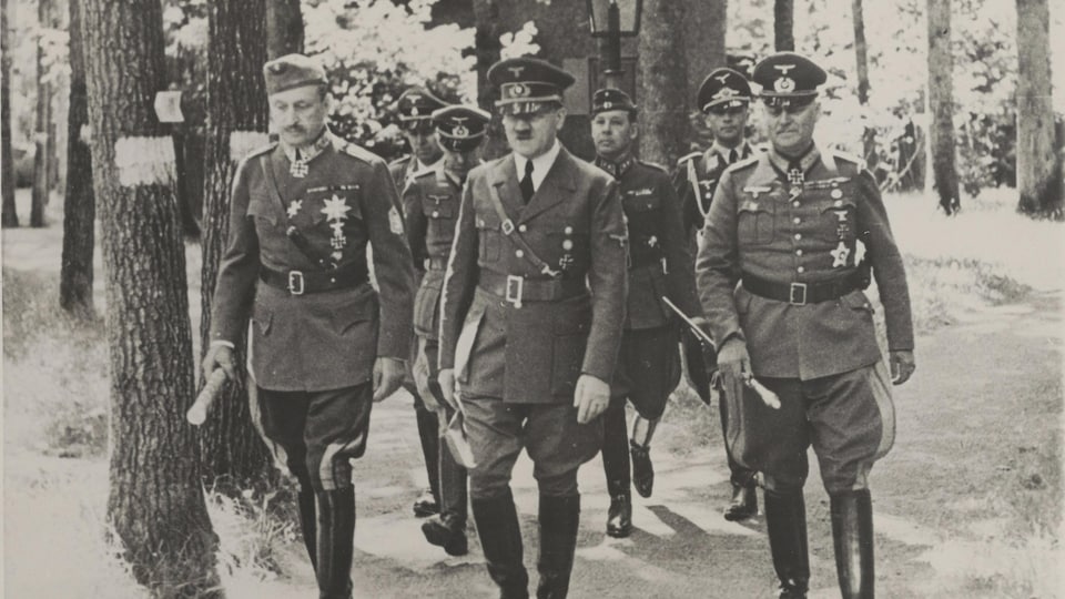 Photo en noir et blanc montrant Adolf Hitler dans une forêt, en compagnie de militaires.