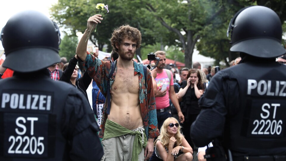 Un homme brandit des fleurs devant des policiers.