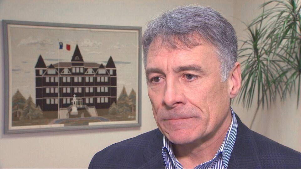 Allister Surette devant un tableau représentant l'Université sur laquelle flotte un drapeau de l'Acadie.