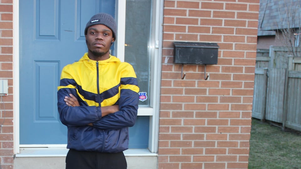 Un jeune homme noir qui porte une tuque devant la porte d'une maison.