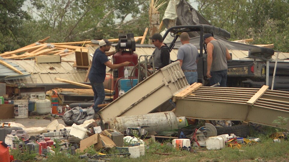 Quatre hommes nettoient les débris d'une maison détruite par le passage de la tornade d'Alonsa