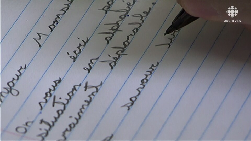 Main qui tient un crayon et qui écrit un texte sur une feuille lignée.