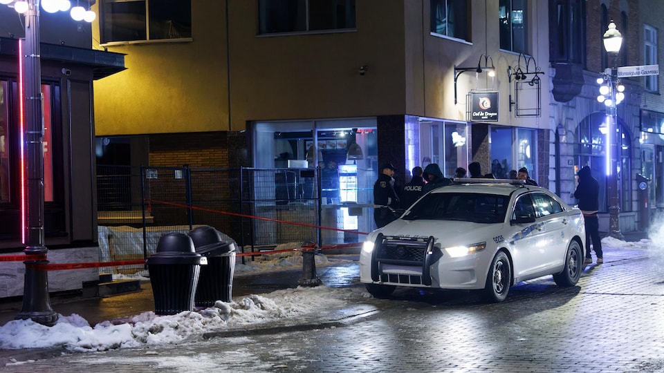 Des policiers discutent près d'une scène de crime, tout près d'une auto-patrouille.