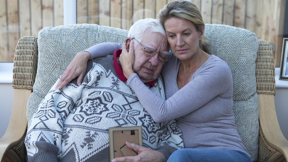 Un homme âgé assis sur le canapé avec sa fille, en regardant une photo.