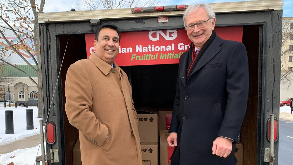 Amarjeet Singh Jatana en compagnie de Blaine Higgs à bord d'un camion dans lequel on peut voir des boîtes de pommes. 