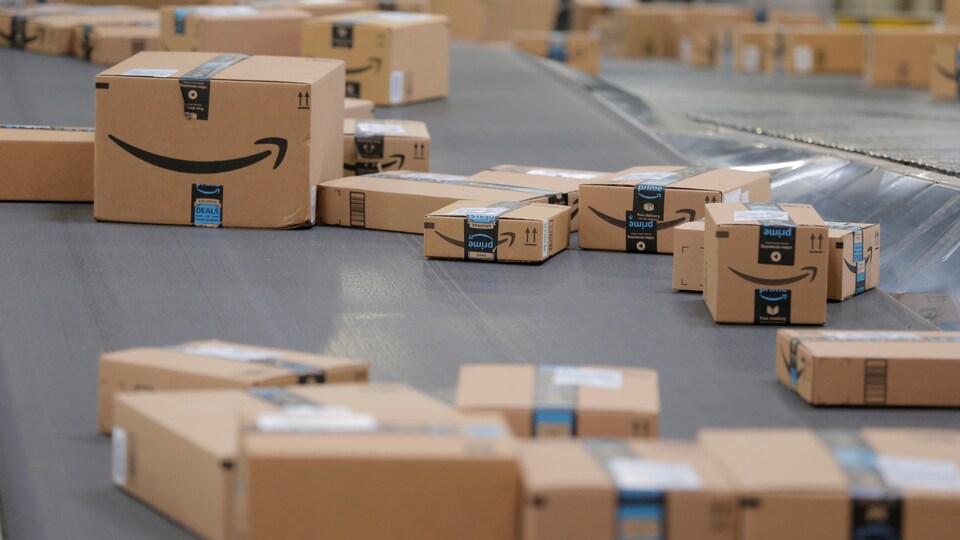 Des boîtes de différentes dimensions avec le logo d'Amazon défilent sur un tapis roulant.