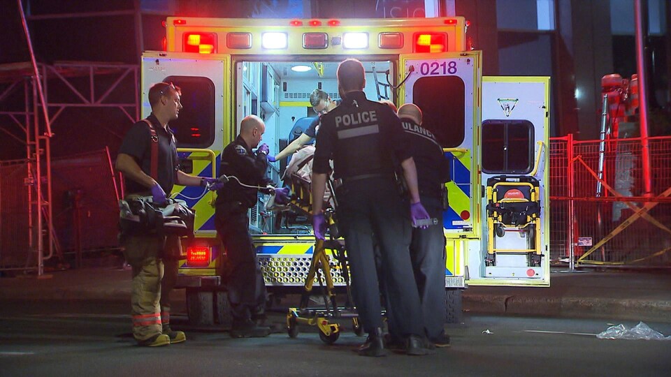 Policiers et ambulanciers entourent la civière qu'on entre dans l'ambulance.
