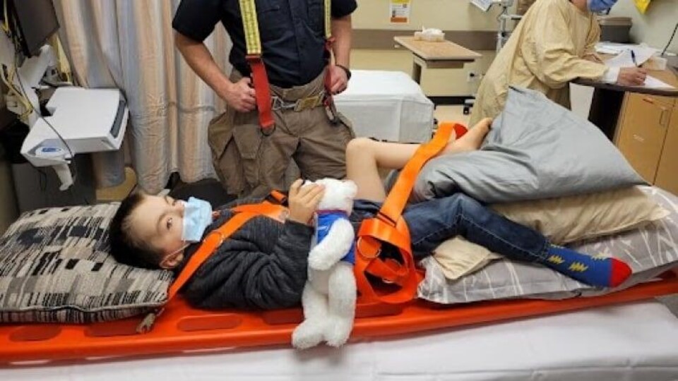 Braden Lousier-Hicks sur un lit d'hôpital avec un pompier à côté.