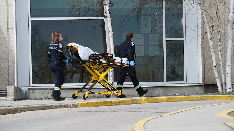 Des ambulanciers conduisent une civière vers l'entrée d'un hôpital.